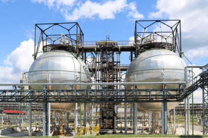 A large round ball-shaped shiny metallic high-pressure iron storage tank for ammonia is strong with pipes and equipment at the petrochemical chemical refinery industrial refinery